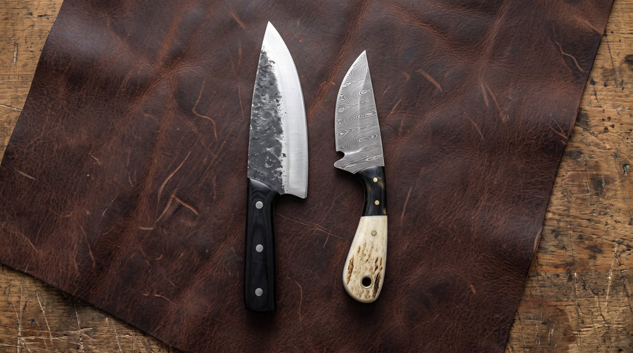 A full tang carbon steel chef knife beside a hidden tang Damascus neck knife with a stag handle on a leather hide